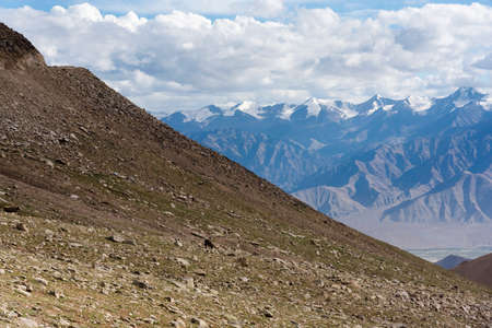 Rocky grass slopes with a view of Himalayan mountains in background in Ladakh, India, Asiaの写真素材