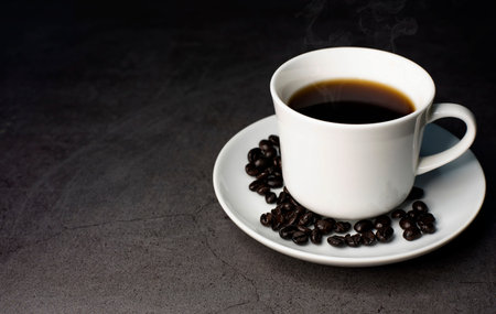 A cup of hot black coffee on a black background with roasted coffee beans and hot steam coming out...