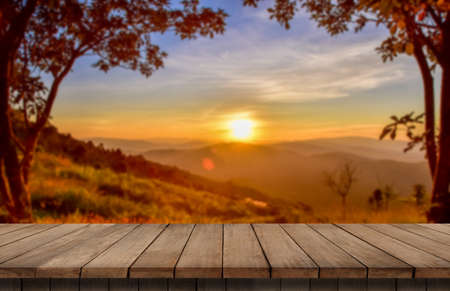 Wooden table and blur of beauty, sunset sky, and mountains as background.の写真素材