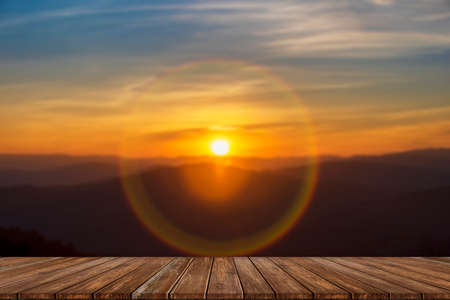 Wooden table and blur of beauty, sunset sky, and mountains as background.の写真素材