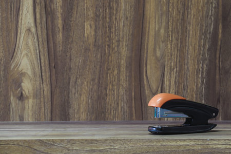 stapler placed on wooden table with copy space for vintage style wood grain background design
