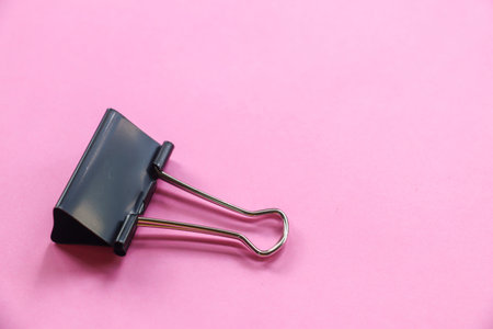 Isolated image of black paperclip paper clip for office paper clip on pink background with copy...