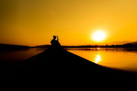 Silhouette of a man sitting on a jetty at sunsetの写真素材