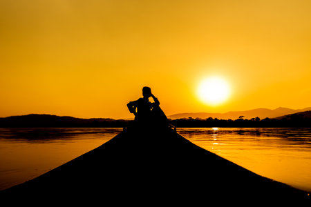 Silhouette of a man and woman sitting on a boat at sunsetの写真素材