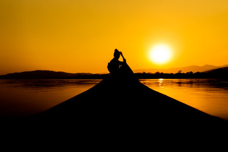 Silhouette of a man sitting on the edge of the river at sunsetの写真素材