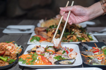 Close up of hand holding wooden chopsticks with shrimps and musselsの写真素材