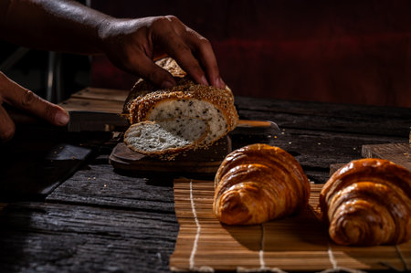 Male hands cutting bread with knife on a wooden table in a bakeryの写真素材