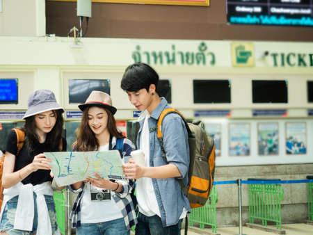 travel concept.group of traveller friend with thai alphabet is trikets counter and time table background.man holding coffee cup and girls ware hat looking map have camera.のeditorial素材