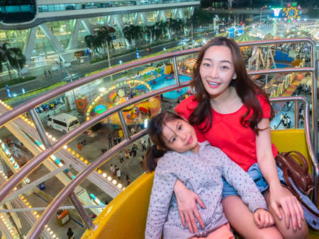 happy asia mother and daughter have fun in amusement carnival park with farris wheel and carousel backgroundの写真素材