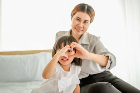 happy family in bed room concept. mother and daugther make heart symbol by hands comfortable bed.の写真素材