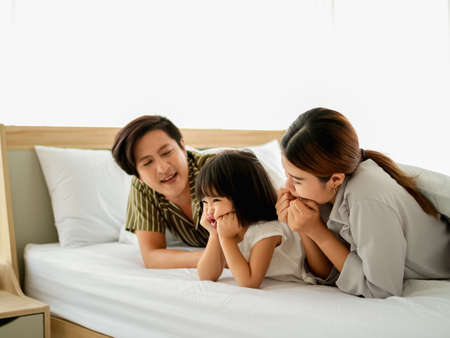 happy family having fun in bed room concept. father,mother and daugther smiling face, kiss love together lying on bed with duvet cover them copy space.の写真素材