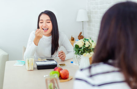 Two beautiful Asian women are sitting and eating new normal lifestyle couple friend use plastic spoon and fork eat foodの写真素材
