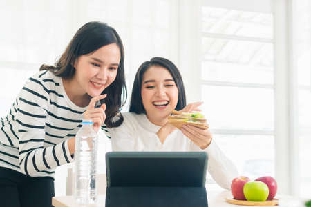 couple asian beauty woman friends sitting eat sandwich. beautiful female smiling and looking tabletの写真素材