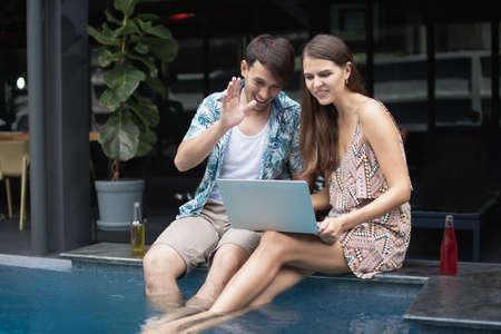 caucasian men and women are doig via video communication through laptop near poolsideの写真素材