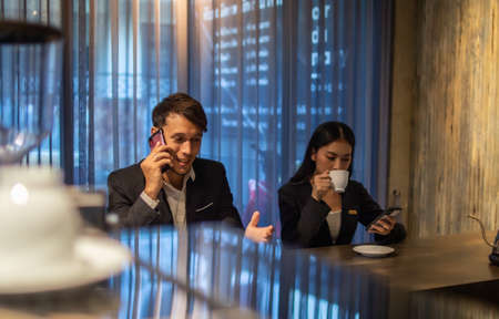 Business men and women drink coffee and use mobile phones in coffee shops in the eveningの写真素材