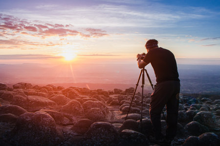 man photographer holding a camera to shoot nature sunrise at mountain scenery.Tourists take pictures of sunset nature with camera on a tripod with copyspace.の写真素材