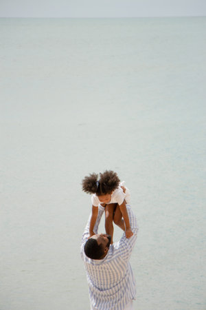 Father holding his daughter up high against sky. african american dady hug girl with sea backgroundの写真素材