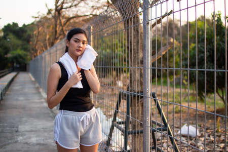asian man jogging and running outdoors in nature. Asian women sweat with a towel after an evening jog.の写真素材