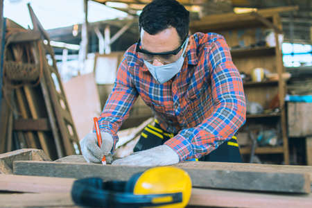 carpenter is working in a woodworking office.caucasion white Carpenter using tape measure to measure distance and marking with pencilの写真素材