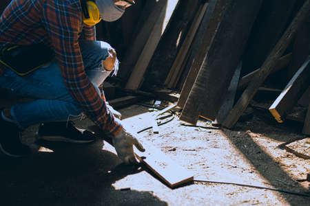 carpenter is working in a woodworking office.A white male carpenter is selecting the wood material and brushing off the sawdust.の写真素材