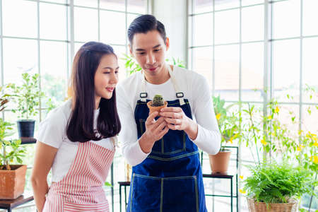 asia entrepreneur beauty woman sitting and holding plant in indoor garden.smiley face gardener wearing apron in plants shopの写真素材