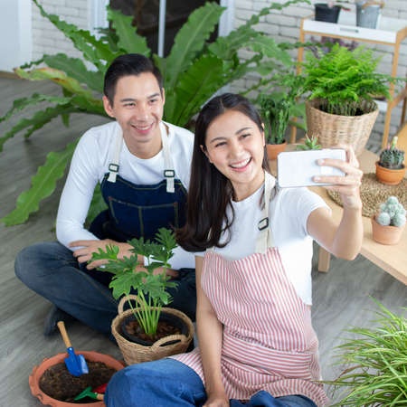 asia entrepreneur beauty woman sitting and holding plant in indoor garden.smiley face gardener wearing apron in plants shopの写真素材