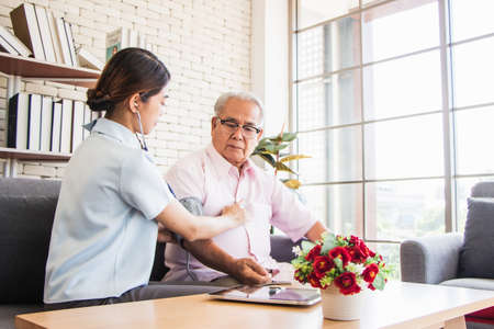 senior man at the nursing home concept. Nurse measures the elderly's blood pressure and pulse at the sitting room at the care center nursing home looking togetherの写真素材