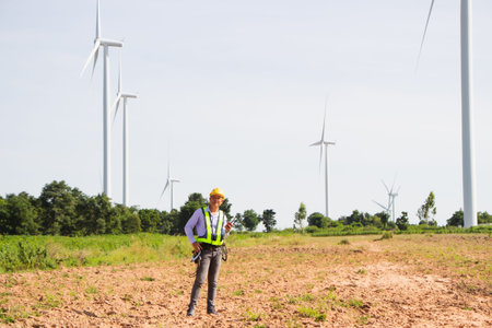 rear view man engineer wearing Personal protective equipment working in wind turbine farm background...