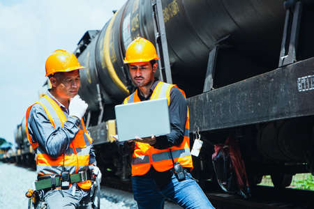 Inspector Engineering wearing helmet and vest worker unifrom checking railway construction work on rail track. Asian worker working on a laptop consulting with a partnerの写真素材