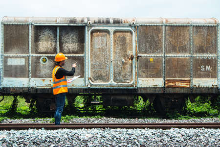 Inspector Engineering wearing helmet and vest worker unifrom checking railway construction work on rail track. Asian workers and coworkers stand beside old train bogies.の写真素材