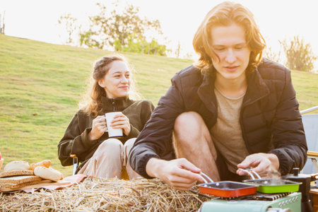 Young couple drinking coffee and playing guitar while camping on their morning vacation.の写真素材