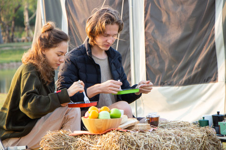 Young couple drinking coffee and playing guitar while camping on their morning vacation.の写真素材