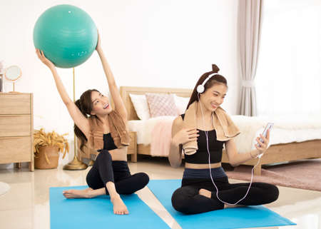 Two beautiful Asian girls wearing workout clothes and smiling with dogs in bedroom. woman on exercise mat with dumbbells and tablet.の写真素材