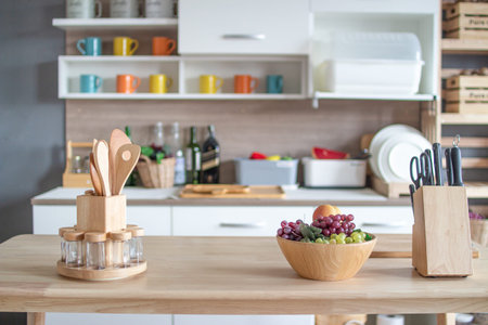 Fruits in a wooden bowl and wooden cutlery on a wooden table with kitchen cabinets in the...