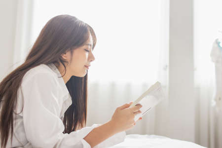Portrait young smile happy beautiful asian woman relax bedroom. Young womanl reading book in morningの写真素材