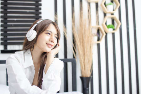 Portrait young smile happy beautiful asian woman relax bedroom. woman with headphones playing acoustic guitar in white bedroom.の写真素材