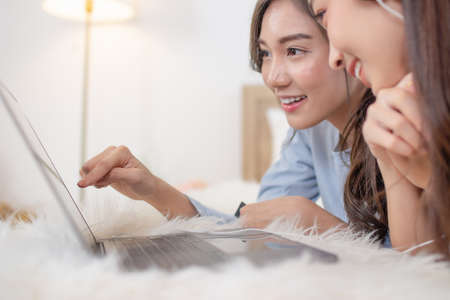 Young asian couple smiling happy using laptop at bedroom. Female friends are happily using credit cards for online shopping.の写真素材