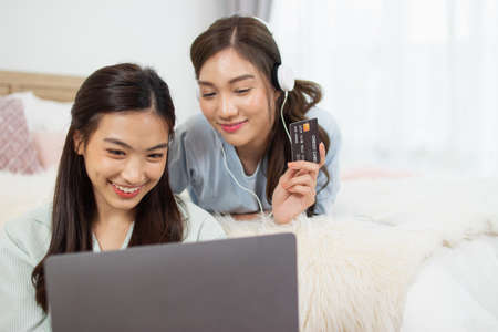 Young asian couple smiling happy using laptop at bedroom. Female friends are happily using credit cards for online shopping.の写真素材