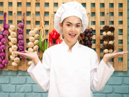 Asian woman in chef's uniform is cooking in the kitchen. portrait female cook smiling with copy space.の写真素材