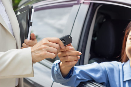 Beautiful young woman car salesman holding car keys and handing it to Asian female customer