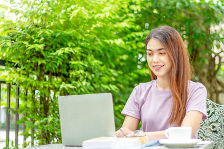 beauty woman doing freelance work in garden. Asian woman using laptop at home back yard with tree background copy spaceの写真素材