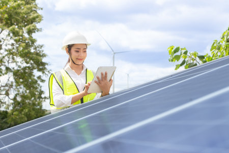 Engineer woman wearing safety helmet and holding blueprint in solar power plantの写真素材