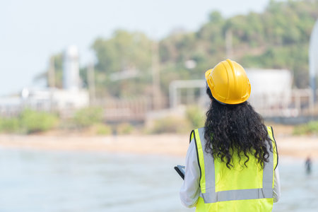 Back view of female engineer with yellow helmet standing on the beach.の写真素材