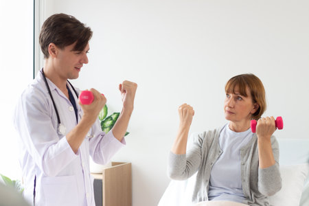 Female patient exercising with dumbbells with physiotherapist at homeの写真素材