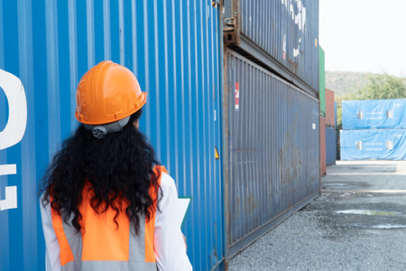 Portrait of a female worker wearing safety helmet and reflective vest looking at the container.の写真素材