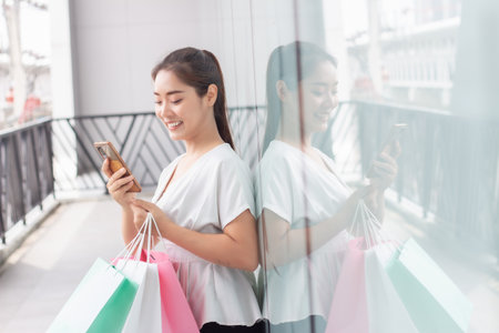 Happy asian woman using mobile phone and shopping bag in shopping mallの写真素材