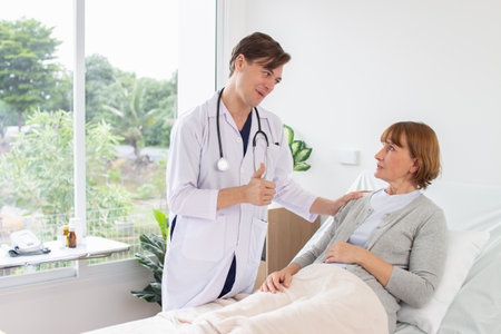 Doctor and patient discussing something while sitting in hospital bed. Focus on womanの写真素材