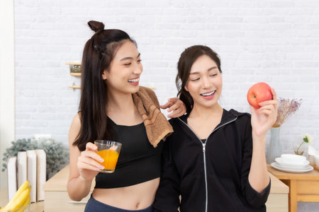 Two asian women in sportswear drinking juice and eating appleの写真素材