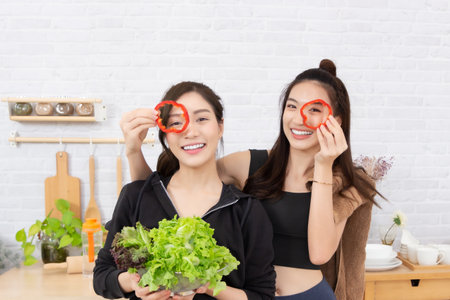Two young asian women holding a fresh salad in the kitchen.の写真素材