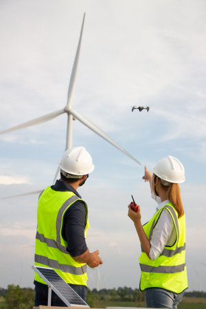 Engineers checking wind turbines in a wind farm. They are wearing safety helmets.の写真素材